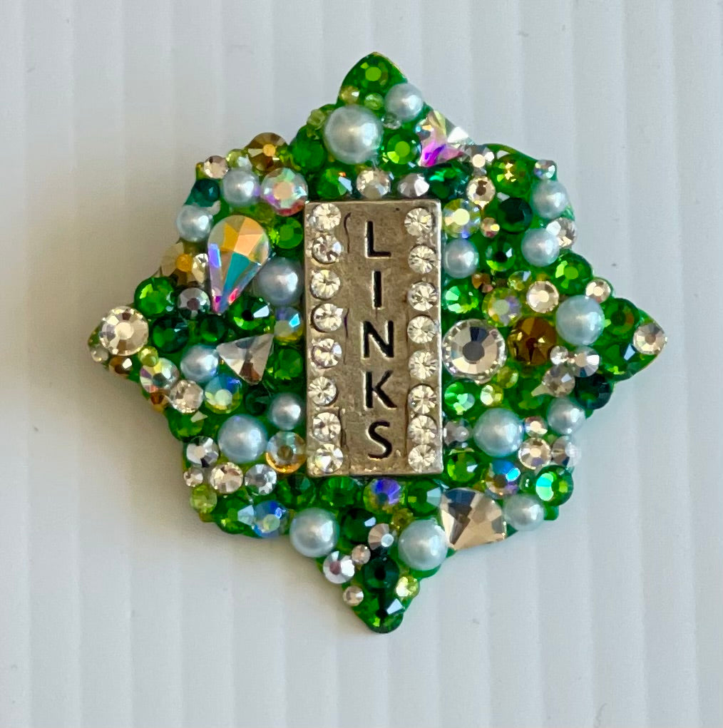 Decorative brooch with green and gold elements on a white background