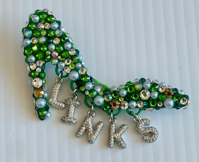 Decorative brooch with green beads and silver charms spelling 'LIVK'S' on a white background