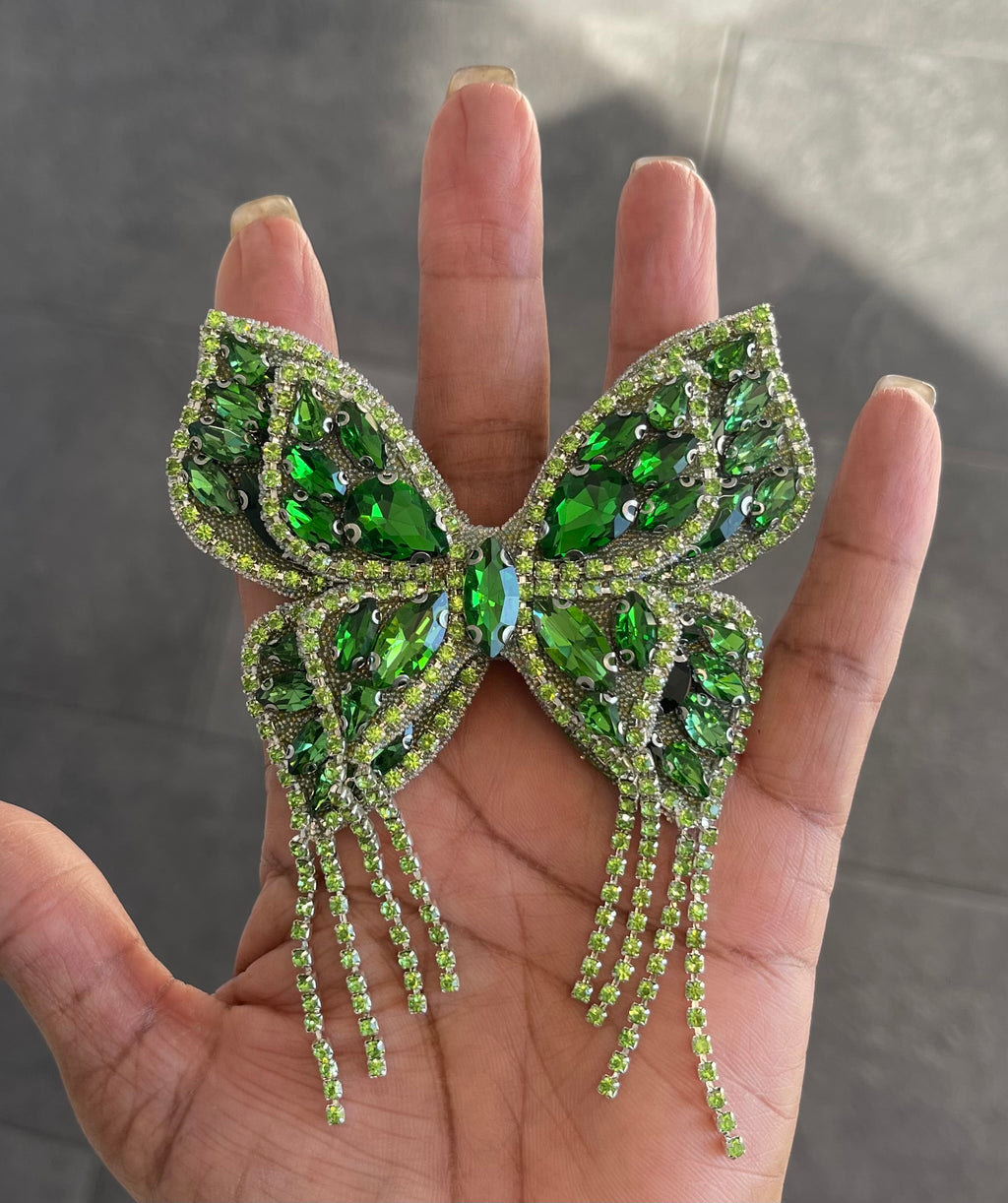 A hand holding a green butterfly-shaped brooch pin adorned with green gemstones and silver accents.