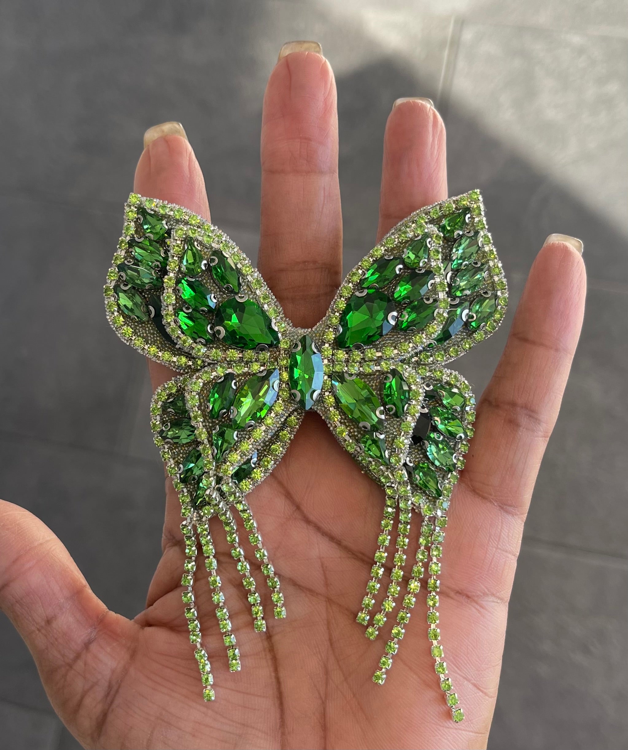 A hand holding a green butterfly-shaped brooch pin adorned with green gemstones and silver accents.
